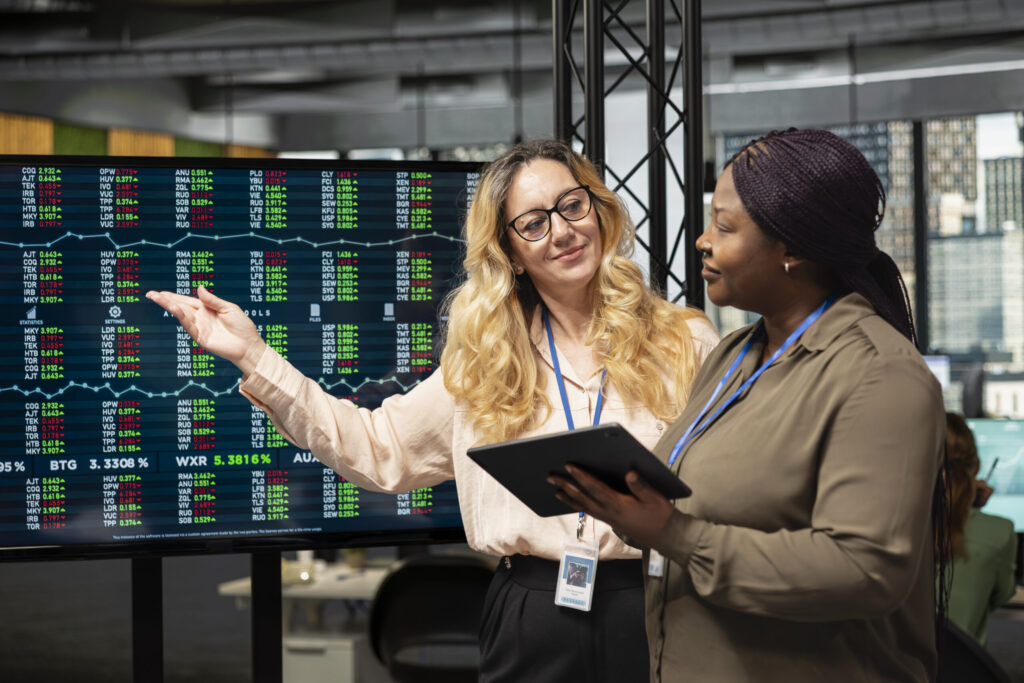 diverse businesswomen working side by side to review data on tv monitor