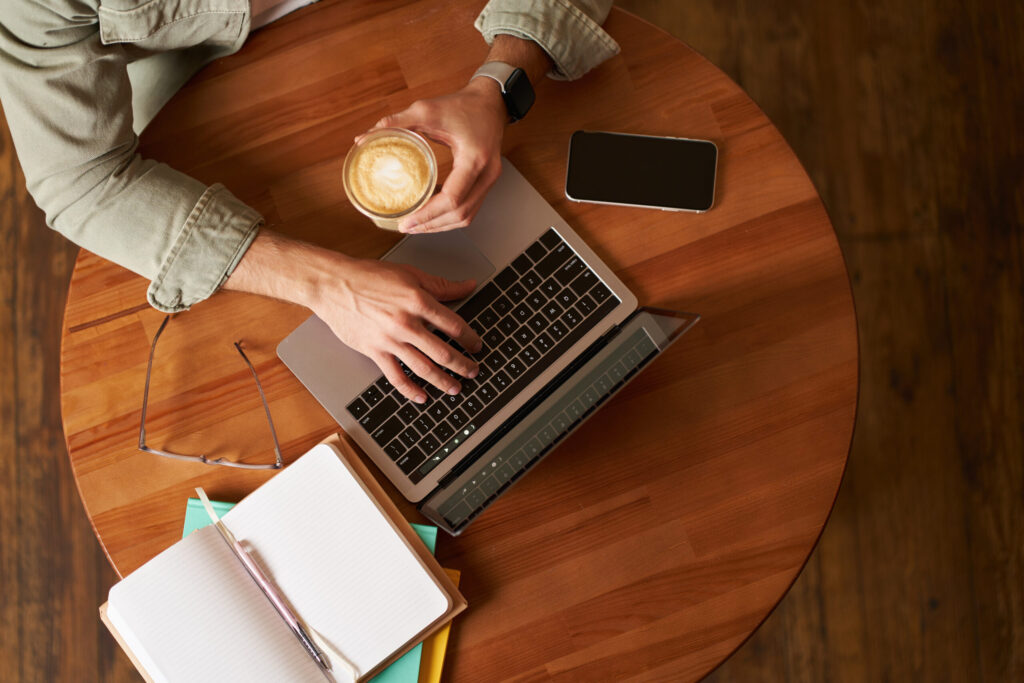 Long-term vs short-term investing: Which is better? co working space, freelance and e learning concept. top view, male hands holding cup of coffee and using laptop. a man sitting in cafe and working or studying online
